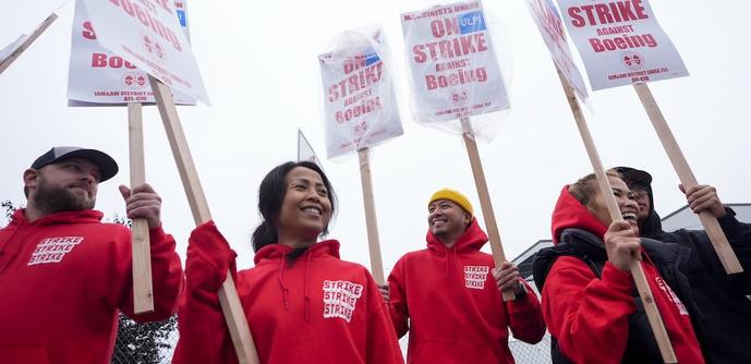IAM machinists union members wearing red STRIKE shirts
 holding picket signs 
ON STRIKE 
against 
BOEING 