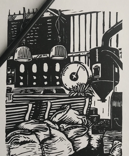 top down photo of a black and white linocut print showing a coffee shop interior with roasting equipment and sacks of coffee beans. A pencil sits atop the print
