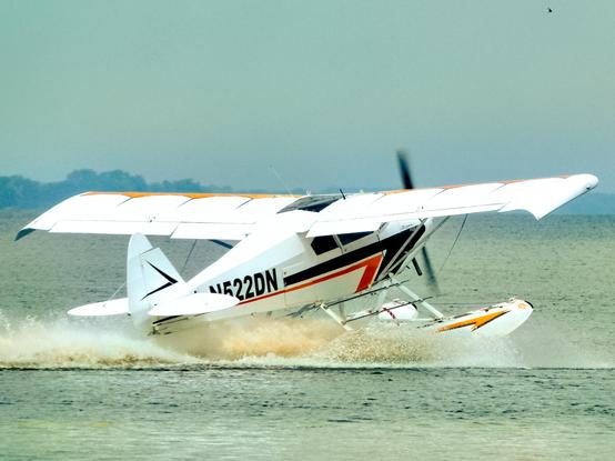 High winged single engined float plane taking off.