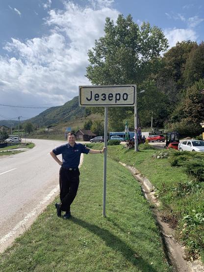The same man, in the same shirt, leaned against the post of a road sign marking the entrance to the town. “Jezero” is written in Cyrillic characters, so “Jезеро”
