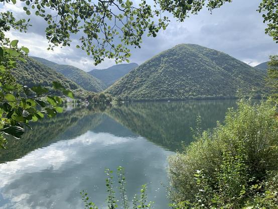 The calm surface of a lake reflects tree-covered hills and clouds