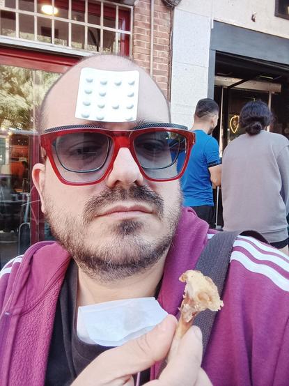 Foto posando con doble gafa ,de ver y roja, y orfidales pegados en la frente. Una alita de pollo devorada en la mano