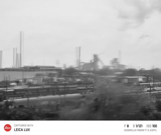 Schwarzweiß Bild eines Hochofenwerks, fotografiert durch eine verregnete Scheibe, wodurch Unschärfe und Hologramme entstanden 