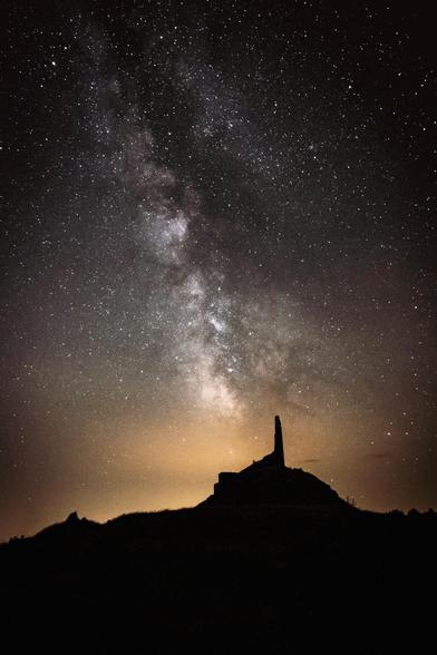 Fotografía nocturna donde en la parte inferior ligeramente a la derecha se puede ver la silueta de una formación rocosa similar a un dedo y en la parte superior el cielo nocturno con la Vía Láctea cortando transversalmente la imagen.