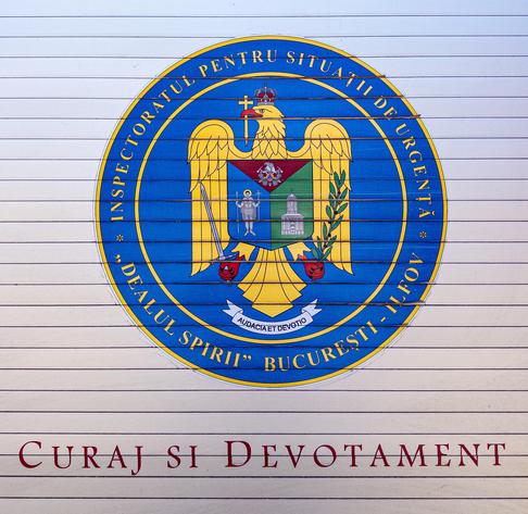 A blue and yellow shield design with an eagle painted on the side of a fire engine, representing the Bucharest firefighting force. There are Romanian words on the shield and underneath.