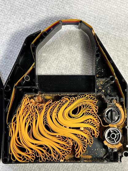 A color ImageWriter II ribbon with top removed showing a color ribbon winding back and forth with crumbling foam pieces distributed everywhere inside. 