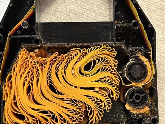Close up of a color ImageWriter II ribbon with top removed showing a color ribbon winding back and forth with crumbling foam pieces distributed everywhere inside. 