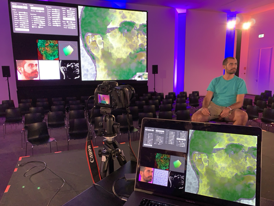 A live demo of a synthetic watercolor portrait painting machine in a big presentation room with colorful lighting and great big LED display sceeens
