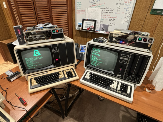 TRS-80 Model 12 computer and Model 16 computer formatting their hard disks.  The covers of both hard disks have been removed.