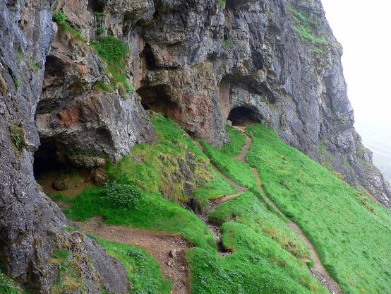 Tres cuevas en un acantilado con caminos rodeado de hierba.