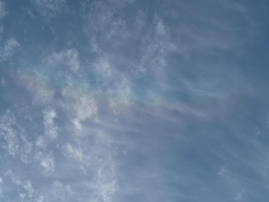 Thin, ragged white clouds on a blue sky, with a faint rainbow colored arc, centered somewhere above the top of the frame