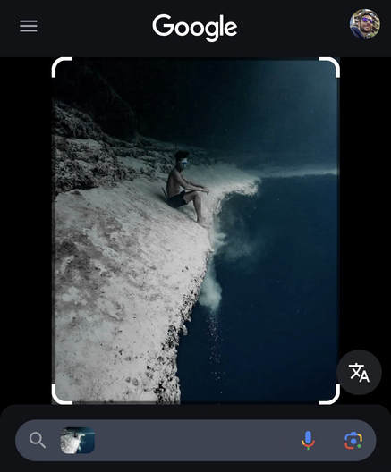 Underwater photo of a person wearing goggles and shorts, sitting on the edge of a steep underwater cliff. The surrounding environment is deep blue and appears murky, with sediment floating around. At the top of the image, a Google search interface is partially visible, including the Google logo, a profile icon, and a translation button.  [Alt text by ALT Text Artist GPT]