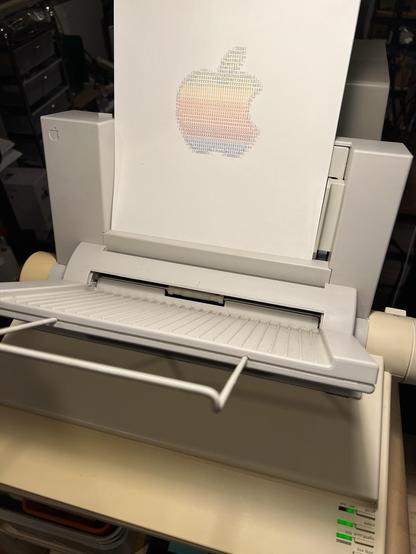 Print of the Apple color logo on paper on top of an ImageWriter II with sheet feeder attachment. 