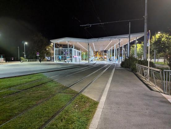 À gauche les rails de tram sont sur gazon, à droite sur béton. La limite marque la frontière entre la France et la Suisse. Au fond la station grandiose de Moillesulaz, porte d'entrée vers la Suisse.