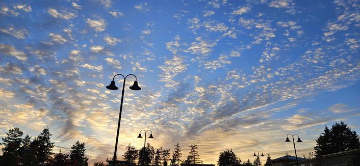 A sunset filled with interesting clouds and droopy two sided street lamps silhouetteed also.