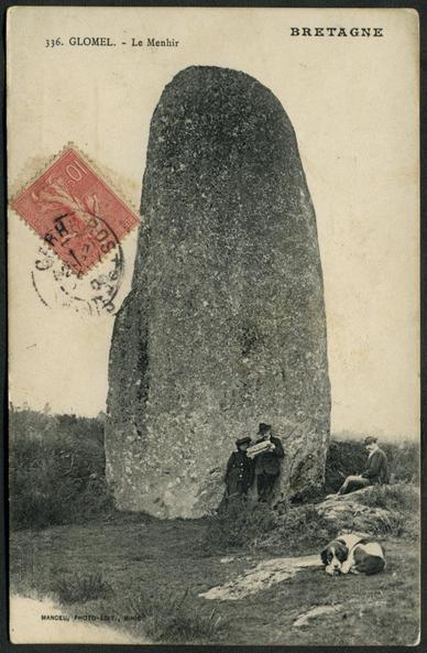A vintage postcard of the Menhir de Glomel at Glomel near Rostrenen in Brittany. A man and woman stand in front of the 9m or 29½ft tall prehistoric standing stone studying a map or possibly a newspaper. Another man is seated on a small rocky outcrop to the right and a dog lies curled up in the foreground. A red 10 cent stamp with Rostrenen postmark is placed at the upper left centre.