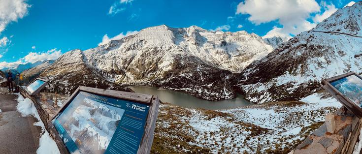 View from the viewing platform onto the Pasterze, Austria's largest glacier. There are informational posters and snow on the surrounding mountain peaks.