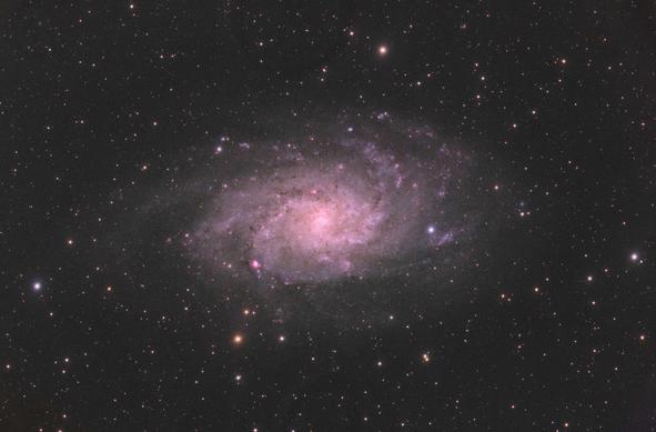 Messier 33: Triangulum Galaxy
Black background with stars of varying brightness and colour spread throughout.

At center is a large spiral galaxy with an orange-ish core. Galaxy disk shape is seen mostly front-on. There are fainter outer white arms with hints of blue, as well as some small dark patches (obscuring dust). The arms contain some small red splotches, which are star-forming regions.
