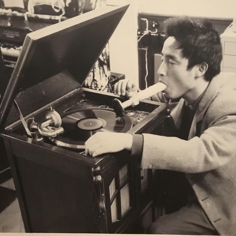 The AI says "A man with short hair plays a recorder while kneeling in front of an old phonograph in a room."