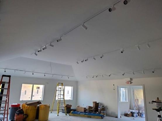 Color photo of new track lighting installed in a white museum exhibit area that's under construction. Ladders, tools and boxes take up the empty space. 