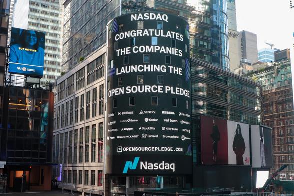 The Nasdaq tower in Times Square showing "Nasdaq congratulates the companies launching the open source pledge", a list of company logos, and opensourcepledge.com.
