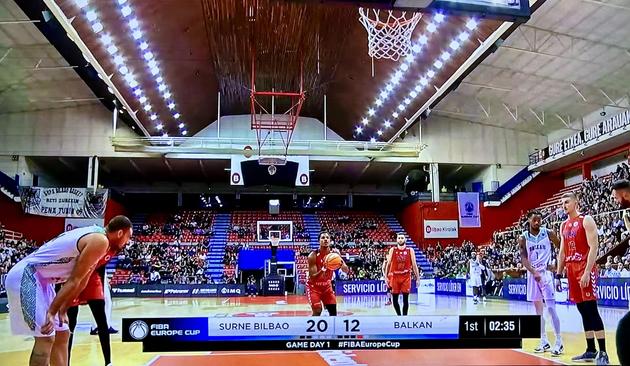 Un partido de baloncesto en curso entre Surne Bilbao y Balkan, con el marcador de 20-12. Un jugador con uniforme rojo se está preparando para hacer un tiro libre.