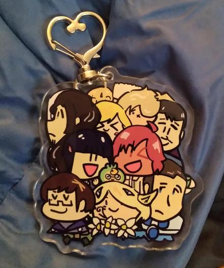 Photo of the reverse side of the charm. Lin (young Asian girl with bobbed hair) and Alexa (smiling red head with tan skin) in the center, along with a tiny potato-like alien (Tatsu, my boy, my son, not to scale). Other playable characters surround them.