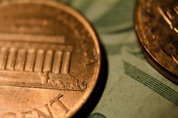 A closeup macro photograph of some coins on a dollar bill. The focus is on a tiny "FG" beside the image on the "tails" side of a penny.