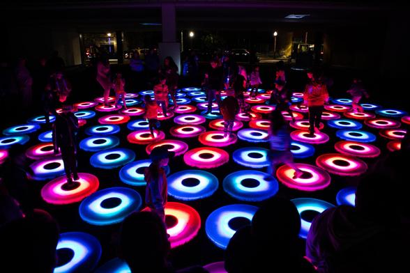 Children playing on lit color-changing pads as part of an installation at Lumenaura. The colors change constantly, but when this image was shot they were mostly blue and pink.