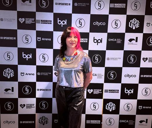 Kat Five in front of the sponsor welcome board at Beyond The Music conference and festival at Factory International, Aviva Studios, Manchester