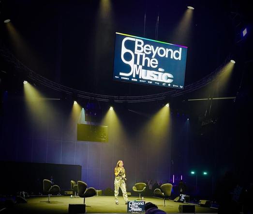 Kat Five with a microphone on stage hosting at Beyond The Music conference and festival at Factory International, Aviva Studios, Manchester