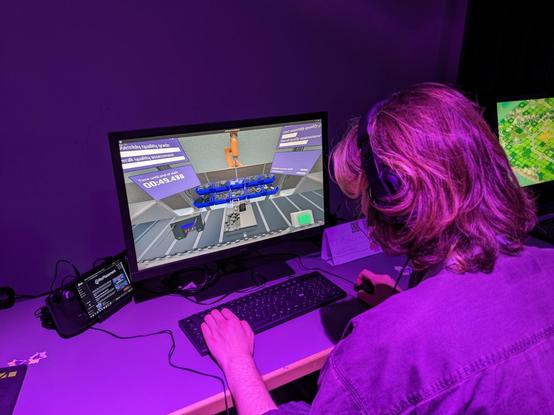 Person sitting at desk with Steam Deck, a monitor, mouse and keyboard, wearing headphones, playing the Re:Placement demo