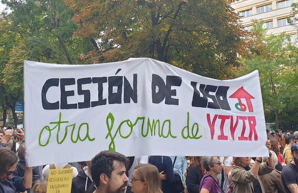 Pancarta en la manifestación con el texto "Cesión de uso, otra forma de vivir" y el logo de un proyecto de viviendas cooperativas en cesión de uso. 