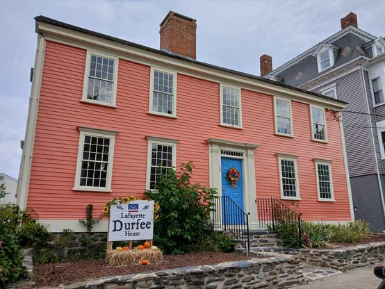 The very salmon colored classic colonial looking house, with a bright blue front door. The door also has a fall wreath in the center. 