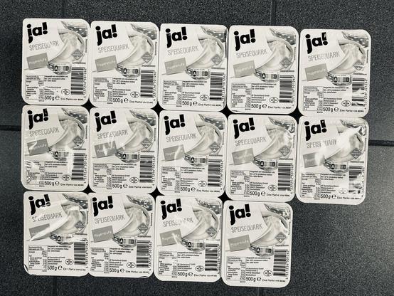 A grid of 16 packages of "ja! Speisequark," a type of low-fat quark cheese, each labeled with product details in German. The packages are uniformly arranged on a dark surface.