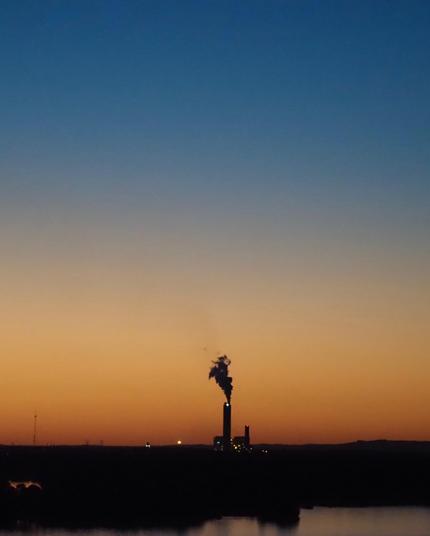 A large smokestack is silhouetted against a sky with sunset colors ranging from orange on the horizon to blue up high.