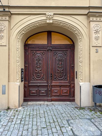 Gelbes Sandsteinfries umrahmt die geschnitzte Holztür