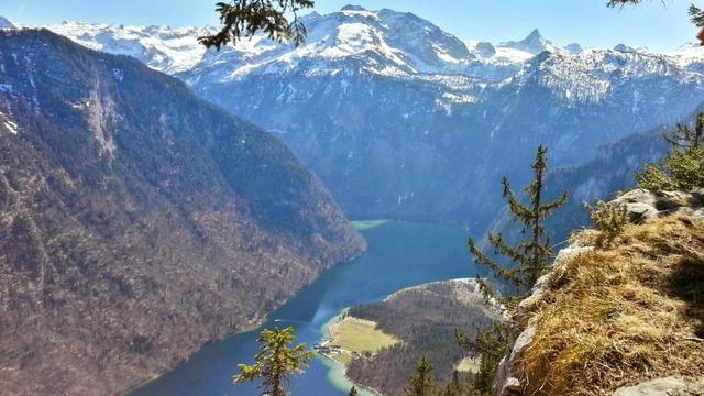 Bildbeschreibung von KI:
Das Foto zeigt eine spektakuläre Berglandschaft mit einem tiefen, türkisblauen See, der sich durch ein Tal schlängelt. Umgeben von steilen, bewaldeten Berghängen ragen im Hintergrund schneebedeckte Gipfel in den Himmel. Der klare blaue Himmel und das Sonnenlicht verleihen der Szene eine friedliche und majestätische Atmosphäre. Die felsige Kante im Vordergrund, auf der der Fotograf möglicherweise stand, bietet einen beeindruckenden Aussichtspunkt auf diese atemberaubende Naturkulisse. Am Ufer des Sees sind kleine Gebäude zu erkennen, die die Einsamkeit und Schönheit dieser Landschaft unterstreichen.