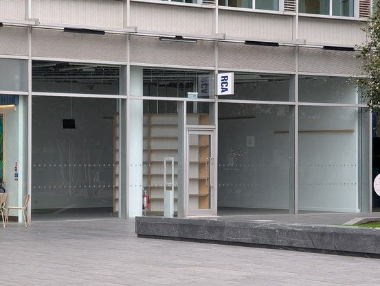 Photo of a shop which has a sign outside it which reads "RCA". The shop is entirely empty aside from a set of (empty) shelves.