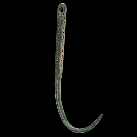 Grünlicher bronzener Angelhaken ohne Widerhaken, am Schaft unter der Öse mit Kreisaugen verziert. 