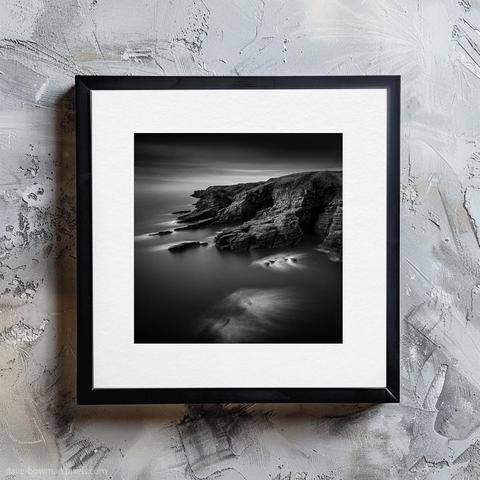 A beautifully framed print titled "Arbroath Cliffs" adorns the wall, showcasing the rugged cliffs of Arbroath in Angus, Scotland, captured in striking black and white. The long exposure technique creates a soft, misty effect in the surrounding sea, contrasting with the sharp, textured contours of the cliffs. This composition emphasises the natural beauty and dramatic lines of the cliffs, inviting viewers to appreciate the enduring strength and timeless appeal of this iconic Scottish landscape.