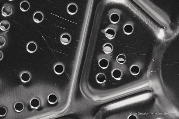 Several small holes in an industrial piece of machinery. Black and white.