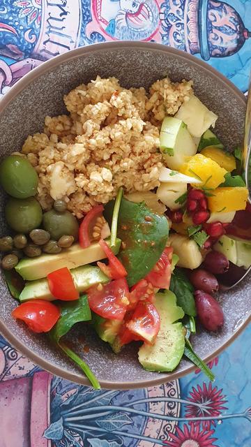 A colourful bowl of raw chopped vegetables, olives and pomegranate