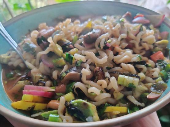 A bowl of ramen, with brightly colored vegetables peeking out happily. There's sunlight illuminating the noodles, so they glisten prettily.