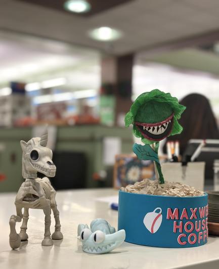 A unicorn skeleton, wiggly worm and miniature Audrey II from Little Shop of Horrors sits on the library checkout counter. 