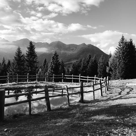 Un piccolo laghetto circondato da uno steccato e le cime delle montagne della Catena delle Maddalene in lontananza