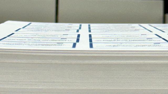 A stack of printed sheets waiting to have individual cards cut out. The shot is taken from along the edge of the stack clearly showing how most of the columns of cards are perfectly aligned, but two cards in one of the columns are shifted slightly to the left, misaligned from the rest.