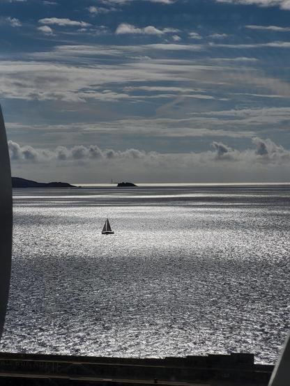 Blick auf das Mittelmeer mit einem kleinen Segelboot am Himmel sind einzelne Wolken. 