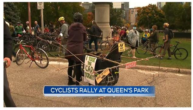 A still from CTV News coverage of the ride and rally for road safety showing me standing beside my cargo bike with a car-sized bamboo frame around it and a sign saying "I TOOK THE CAR TODAY"