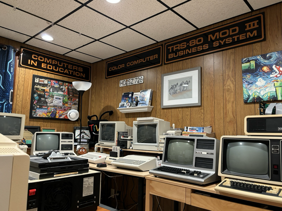 Photo showing various computers from the the 1980s with brown signs in the background advertising various Radio Shack computers.